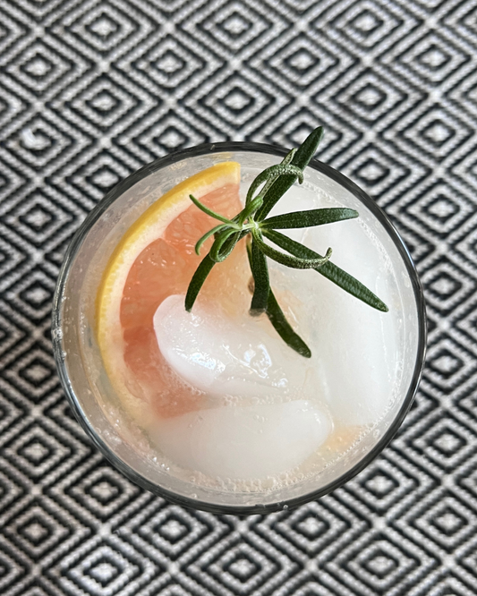 An overhead photo of a glass filled with a Rosemary Grapefruit Spritz, garnished with a slice of grapefruit and spring of rosemary.
