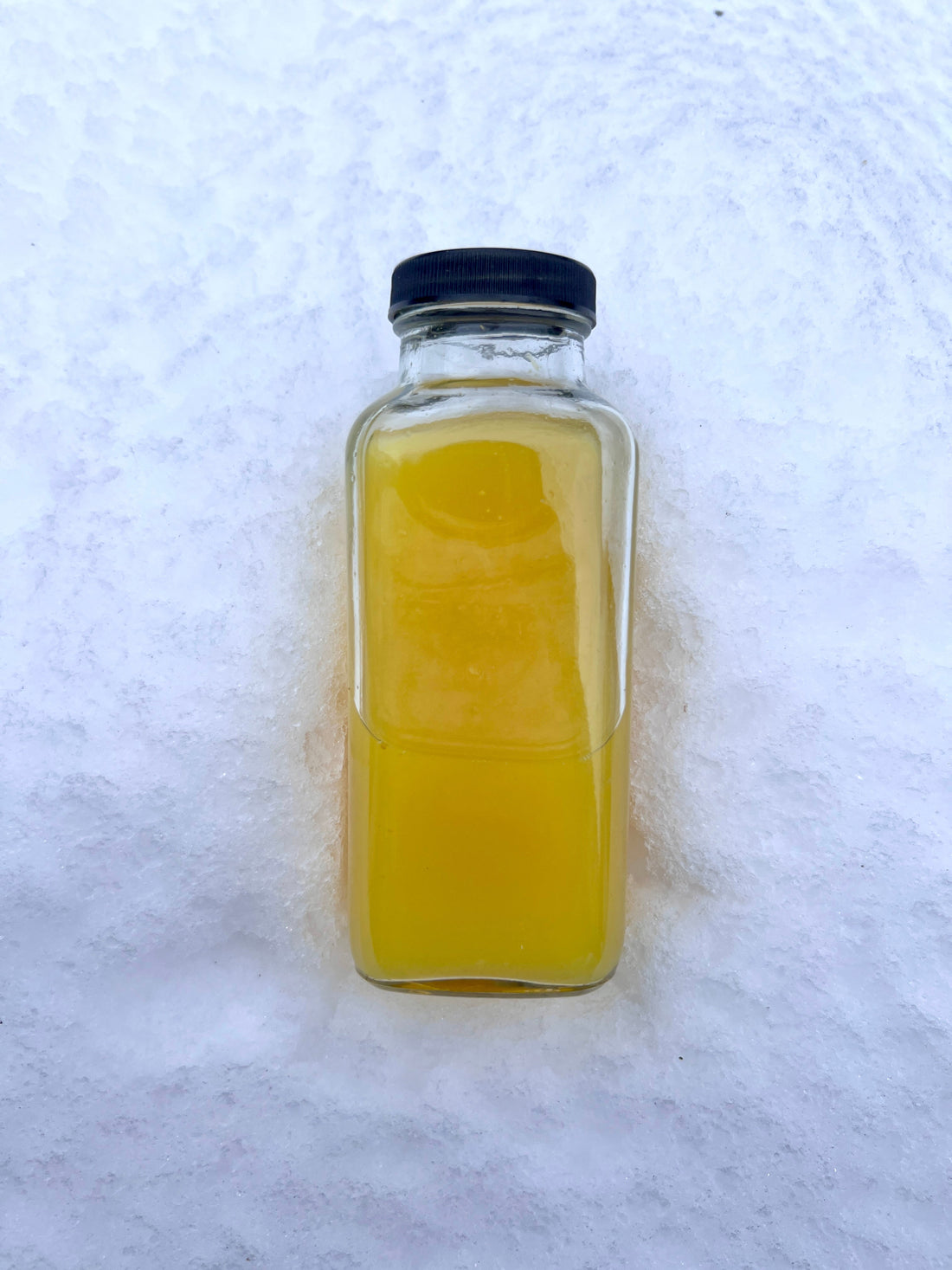 Glass jar filled with golden ginger turmeric switchel sitting in fresh snow.
