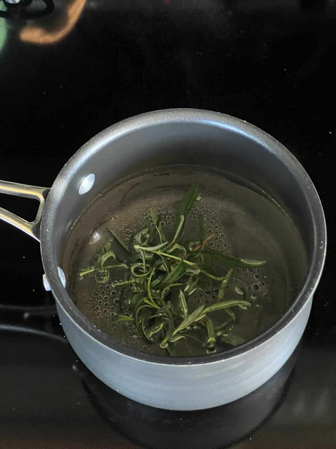 Rosemary simmers in a simple syrup base in a black pot on the stove.