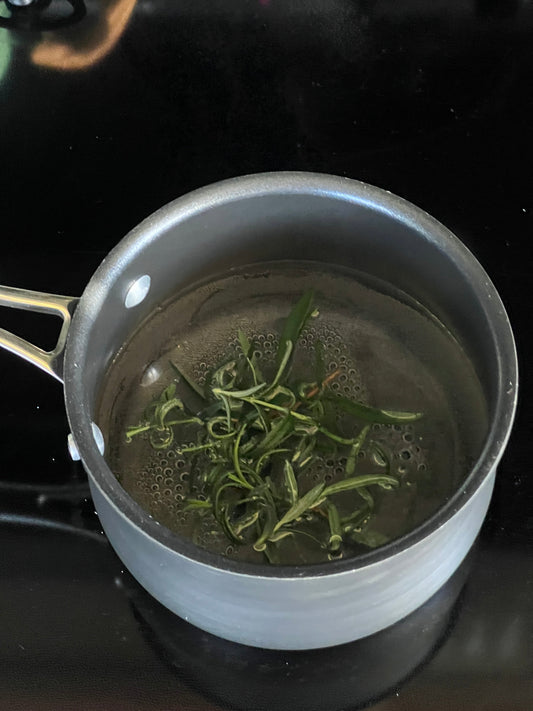 Rosemary simmers in a simple syrup base in a black pot on the stove.
