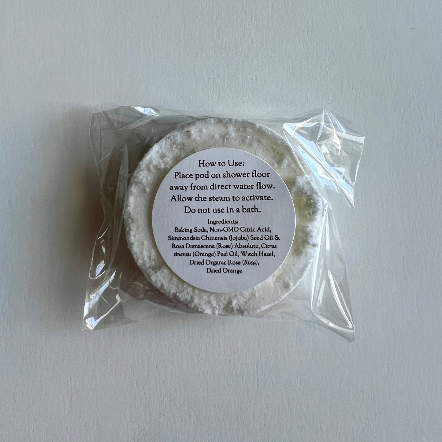 Bath salt pod in clear packaging with a label on a light gray background