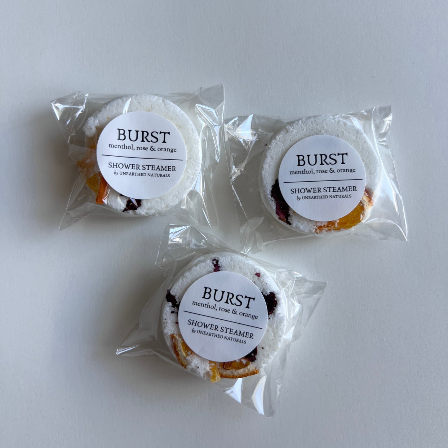 Three small round packaged shower steamers with 'Burst' labels on a white background