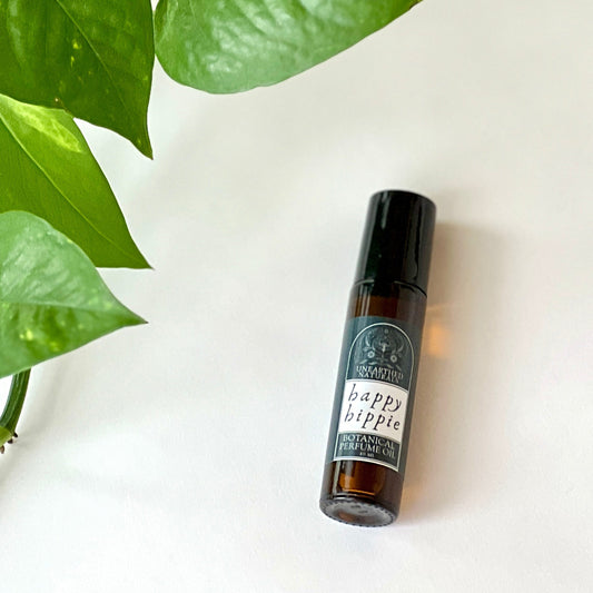 Happy Hippie roller ball lays on a white background with green pothos leaves. 